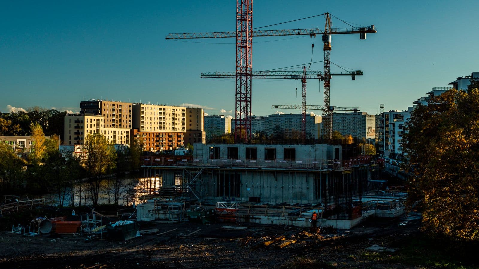 Tower cranes over the concrete frame of a building under construction at dusk.