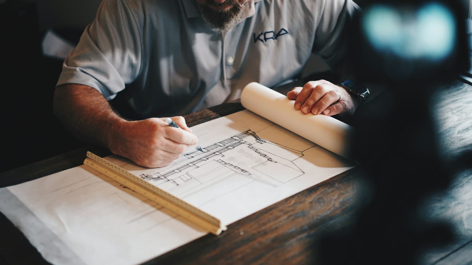 A design engineer marking up a building elevation drawing at a drafting desk.
