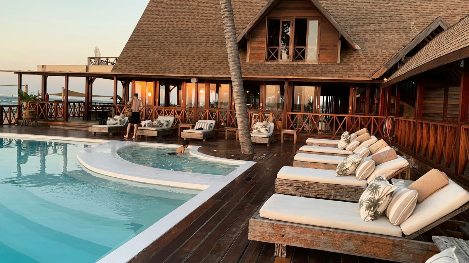 The pool deck and terrace of a beachfront resort at sunset.